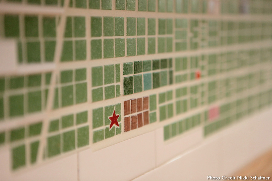 Close-up of the 1842 Cincinnati map mosaic — green glass tile street grid with notable historic buildings highlighted as colored accent tiles including a red star, mahogany window grid, and teal block
