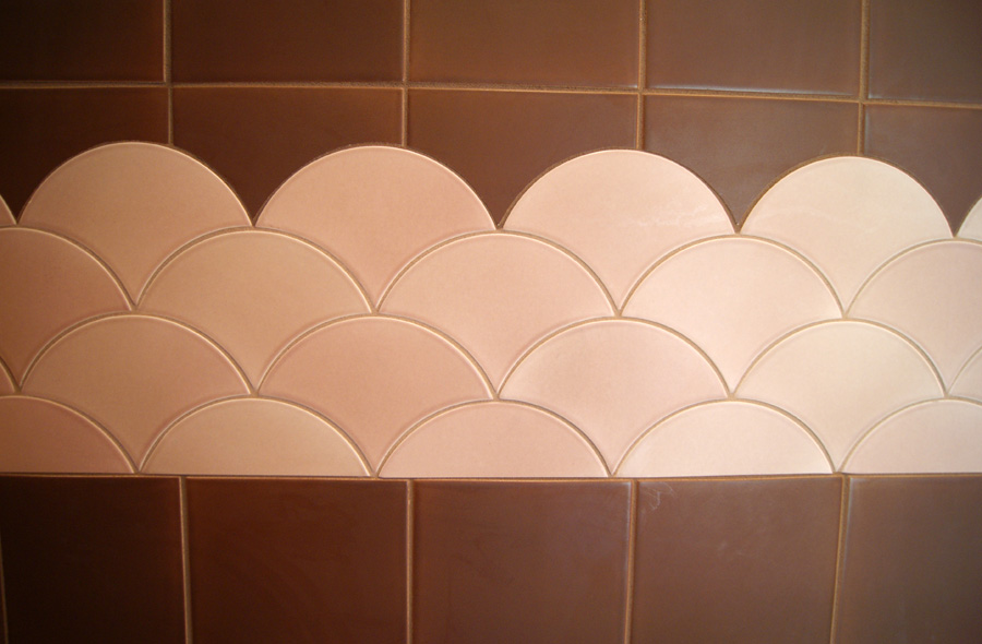 Close-up of pink scalloped fish-scale tile band trim transitioning between brown porcelain tile fields