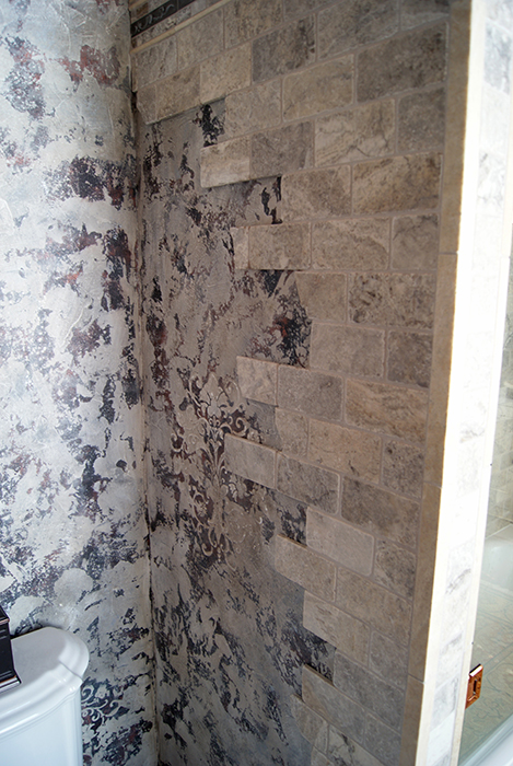Detail of the "falling stones" tile effect — gray stone tile bricks tumbling irregularly from a damask-wallpapered corner into the main stone tile field
