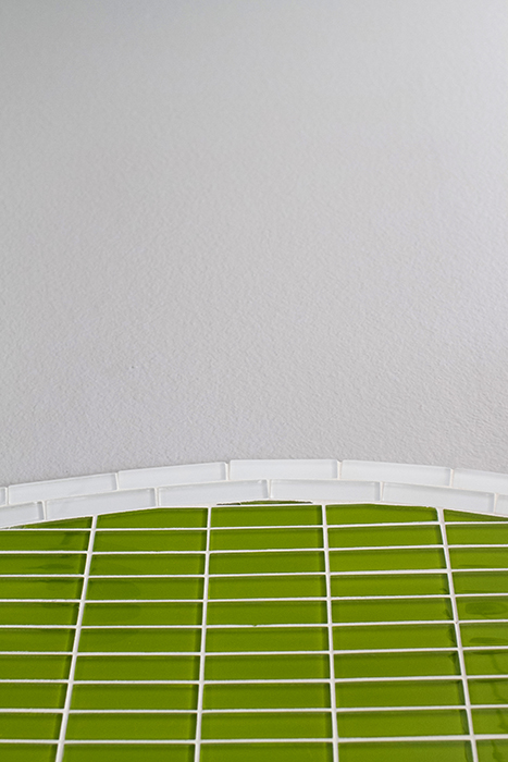 Detail of the top of an arched tile feature — lime green vertical linear glass mosaic meeting a painted wall, with a small white tile cap row tracing the arc