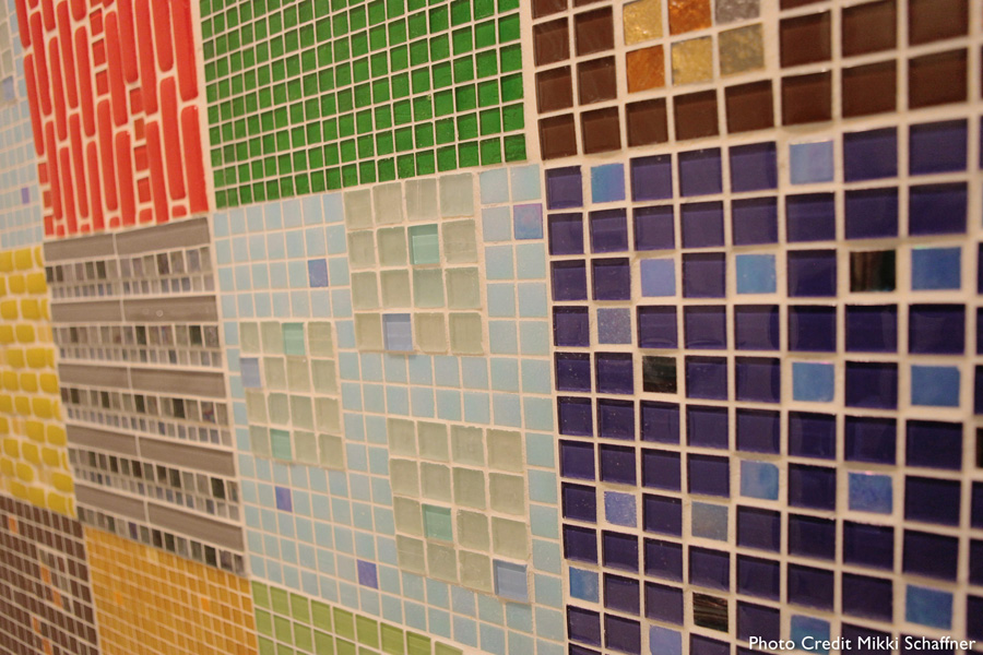 Close-up of a patchwork "quilt" mosaic — squares in varied colors and patterns including red brick, green grid, brown with yellow accents, blue with light squares, gray, and yellow, each patch a different tile composition