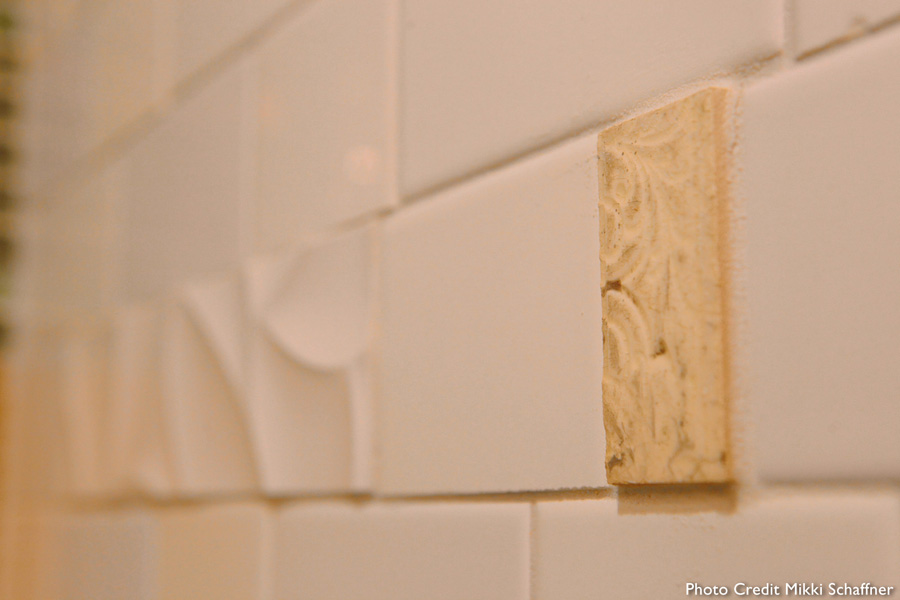 Close-up of decorative wave-and-ribbon bas-relief subway tile detail with a small carved travertine accent inset