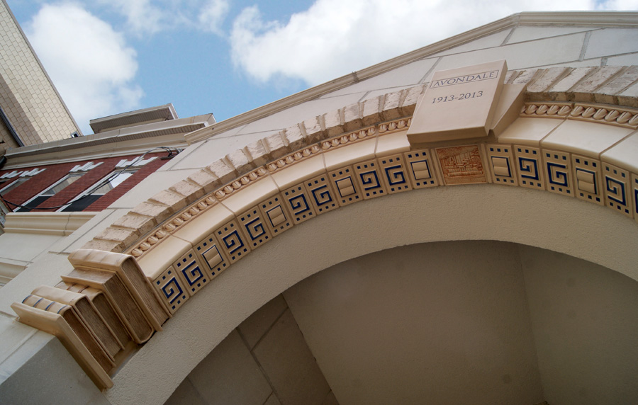 Arched library entry with a Rookwood tile Greek key band, dentil molding, "Avondale 1913-2013" keystone block, columned corbel supports, and a smaller terracotta-relief tile depicting a historic building