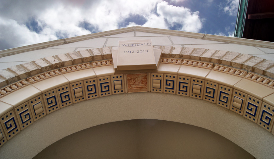 Library entry keystone view — "Avondale 1913-2013" cornerstone block above a Rookwood tile band of Greek key pattern with a small terracotta-relief tile of a building, framed by egg-and-dart molding