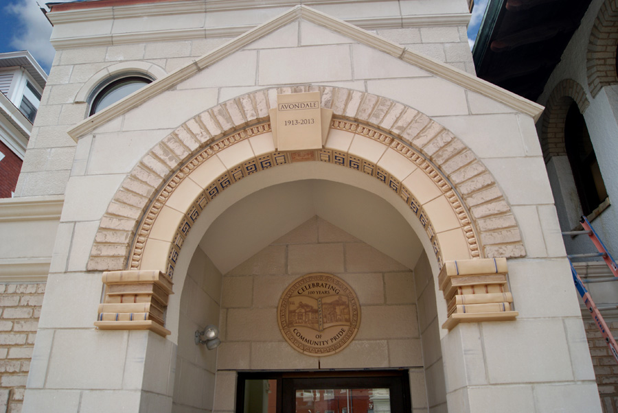 Full façade of the Avondale Branch Library entry — limestone pediment, arched entrance with Rookwood tile detail, and a circular ceramic centennial medallion mounted above the door