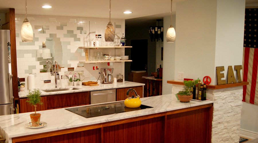Modern kitchen with white subway tile backsplash featuring scattered pale blue and gray accent tiles, marble countertops, walnut cabinets, and glass pendant lighting