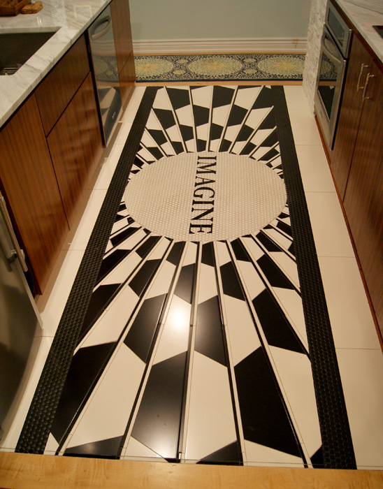 Overhead view of a black-and-white starburst floor mosaic between kitchen cabinets, with central "IMAGINE" medallion in tribute to the Strawberry Fields Memorial