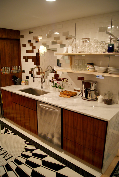 Galley kitchen with white subway tile backsplash featuring small mahogany and mirror accent tiles, marble counter, walnut cabinets, stainless dishwasher, with the "IMAGINE" floor mosaic visible in the foreground