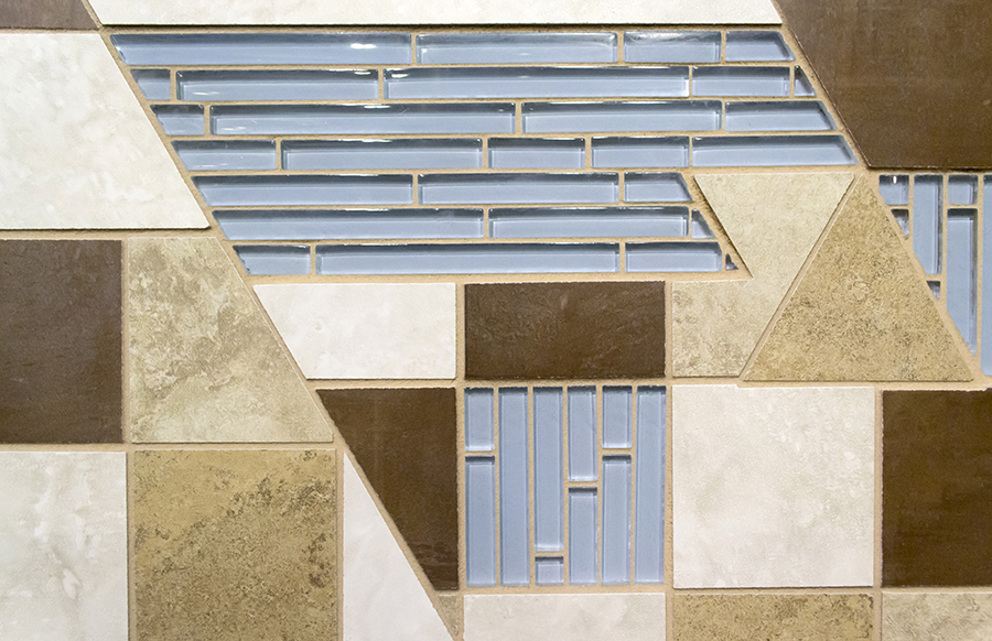 Mosaic detail with iridescent blue glass brick tile against stone-look ceramic tile in tans, browns, and cream, arranged in geometric panels