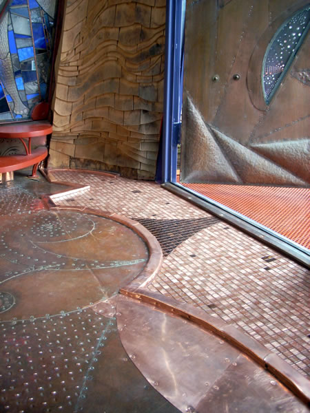 Entryway floor of copper-tile and copper-clad flowing shapes, meeting a shingled wood accent wall in the background