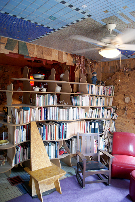 Sculptural curved wood bookshelves in a library nook beneath a deep blue mosaic-tiled ceiling, with a Craftsman chair and ceiling fan