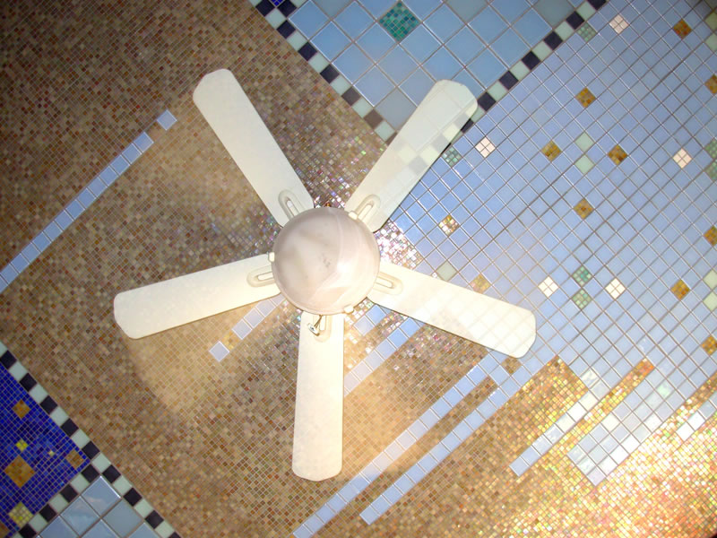 Ceiling fan set against iridescent glass mosaic tile in pink, gold, tan, and blue with diagonal grid patterns