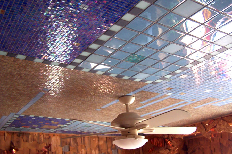 Wide view of a mosaic-tiled ceiling with a white ceiling fan light, iridescent cobalt, tan, and pink glass tile panels overhead