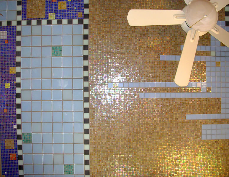 Mosaic ceiling detail with a partial ceiling fan view — gold iridescent tile meets blue gridded panels with multicolor accent tiles