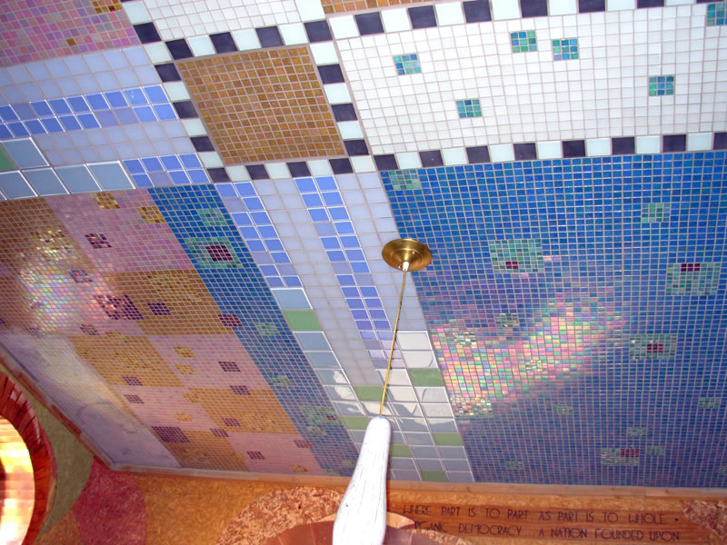 Mosaic-tiled ceiling with a brass pendant lamp hanging on a long rod over an inscribed wood beam