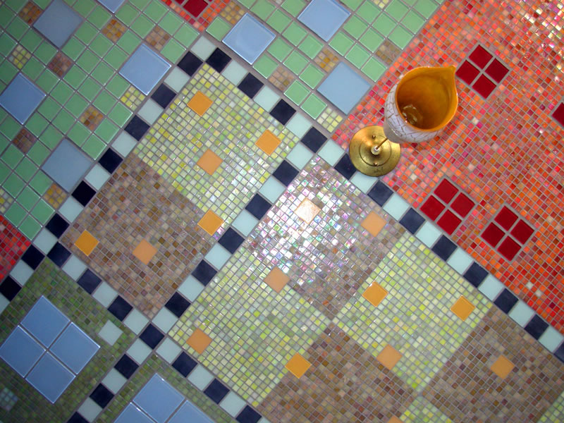 Detail of mosaic ceiling panels meeting at corners — pale green, light blue, salmon, and yellow-green tile with regular square accents and checker borders