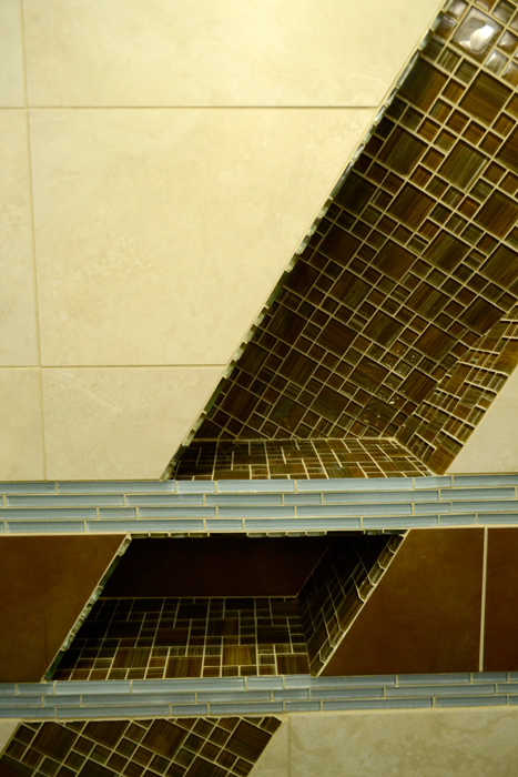 Sloped tile niche cut into the shower wall, lined with brown striped glass mosaic and trimmed with pale blue glass linear tile