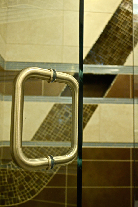 Brushed chrome shower door handle with the brown glass mosaic wave pattern visible through the glass beyond